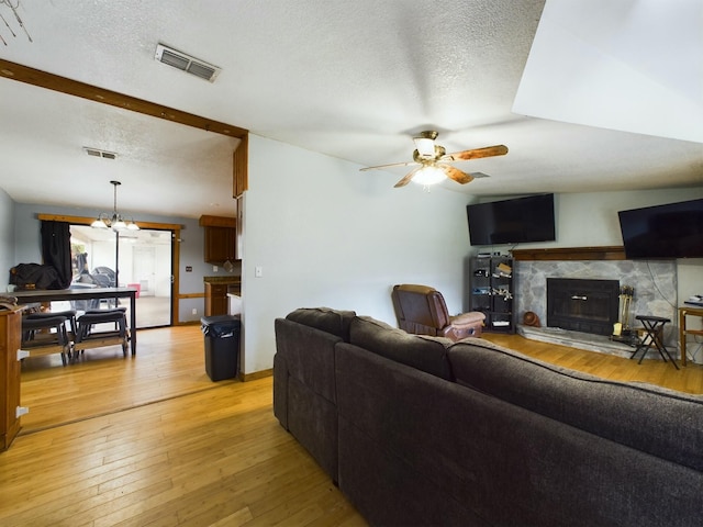 living room featuring ceiling fan with notable chandelier, a textured ceiling, a fireplace, and light hardwood / wood-style flooring