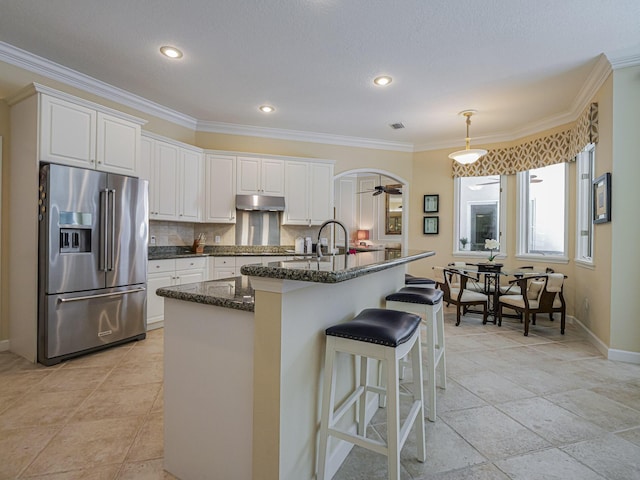 kitchen featuring tasteful backsplash, an island with sink, white cabinets, dark stone counters, and high end fridge