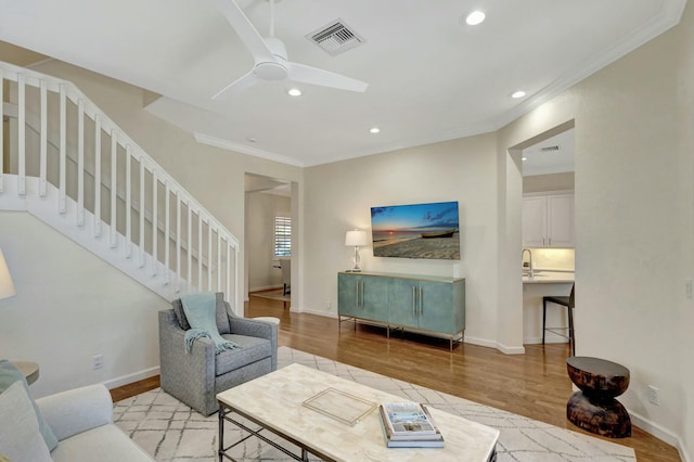 living room featuring ceiling fan, ornamental molding, and light hardwood / wood-style floors