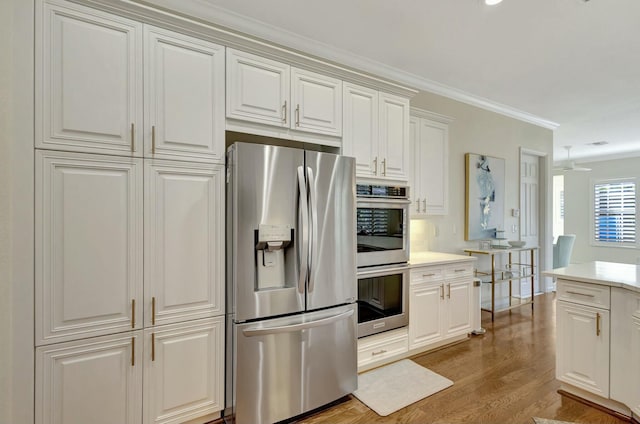 kitchen featuring light wood-type flooring, ornamental molding, appliances with stainless steel finishes, ceiling fan, and white cabinets