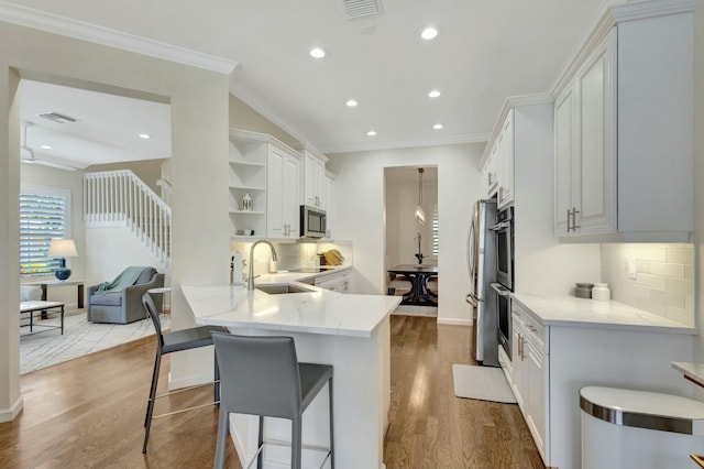 kitchen featuring a breakfast bar, sink, light wood-type flooring, kitchen peninsula, and white cabinets