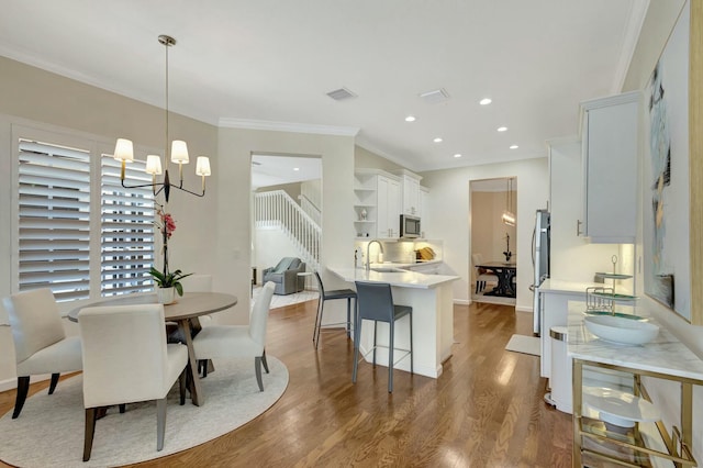 dining room with wood-type flooring, sink, a notable chandelier, and crown molding