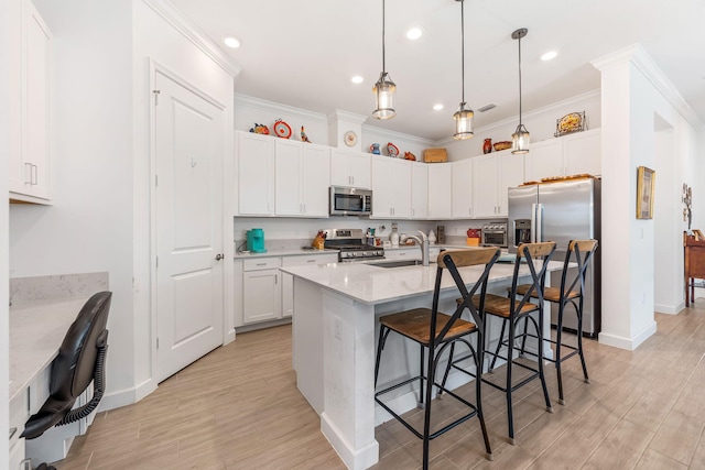 kitchen with a breakfast bar area, white cabinetry, decorative light fixtures, a center island with sink, and appliances with stainless steel finishes