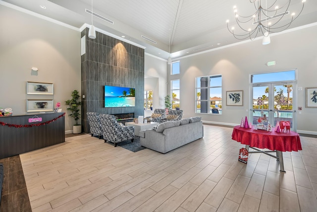 living room featuring a towering ceiling, a fireplace, ornamental molding, light wood-type flooring, and french doors