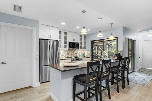 kitchen featuring a breakfast bar area, dark stone countertops, appliances with stainless steel finishes, pendant lighting, and white cabinets