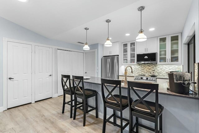 kitchen with appliances with stainless steel finishes, pendant lighting, white cabinetry, backsplash, and light hardwood / wood-style flooring