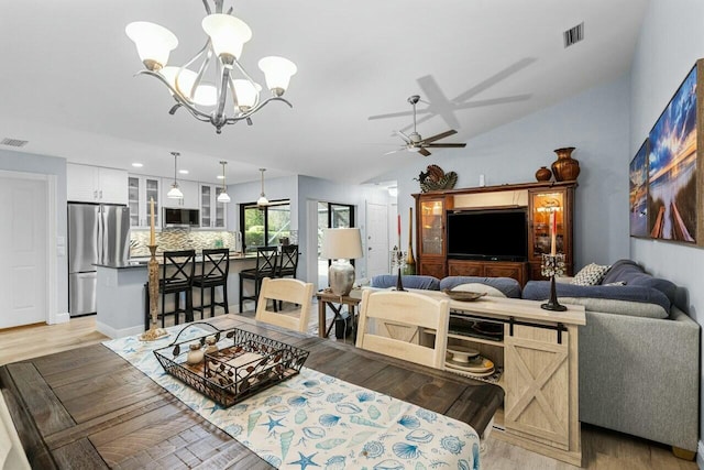 dining area with vaulted ceiling, ceiling fan with notable chandelier, and light wood-type flooring