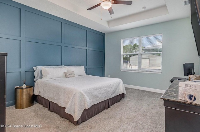 bedroom featuring ceiling fan, light colored carpet, and a tray ceiling