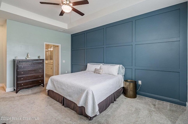 bedroom with a tray ceiling, light colored carpet, ceiling fan, and ensuite bathroom