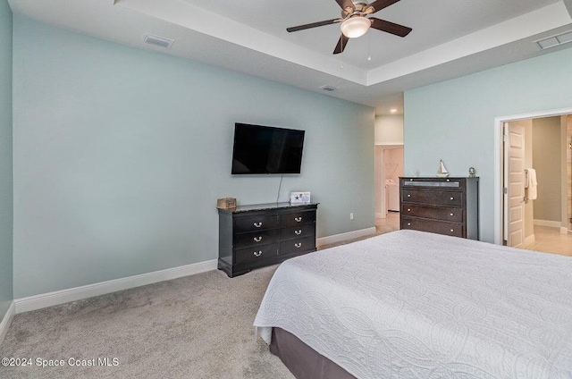 carpeted bedroom with a tray ceiling, ceiling fan, and ensuite bathroom