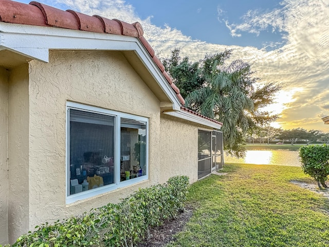 property exterior at dusk featuring a water view and a lawn