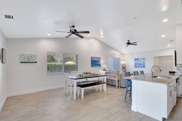 kitchen with lofted ceiling, sink, light stone counters, light hardwood / wood-style floors, and white cabinets