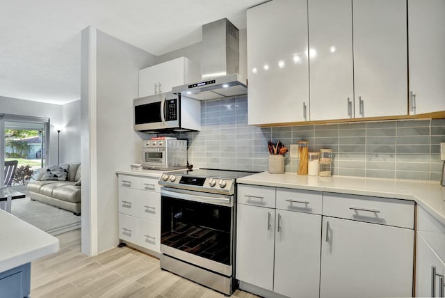 kitchen featuring tasteful backsplash, wall chimney range hood, stainless steel appliances, light hardwood / wood-style floors, and white cabinets