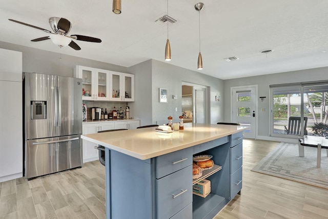 kitchen featuring decorative light fixtures, white cabinets, stainless steel fridge, a center island, and light hardwood / wood-style flooring