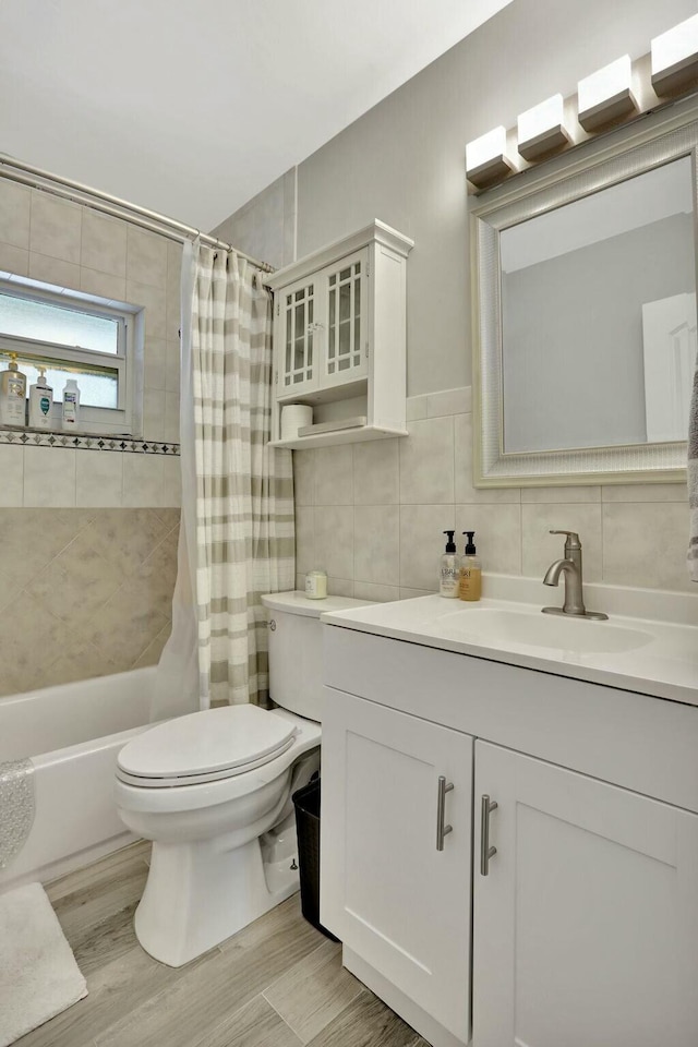 full bathroom featuring hardwood / wood-style floors, tile walls, shower / bath combination with curtain, vanity, and toilet