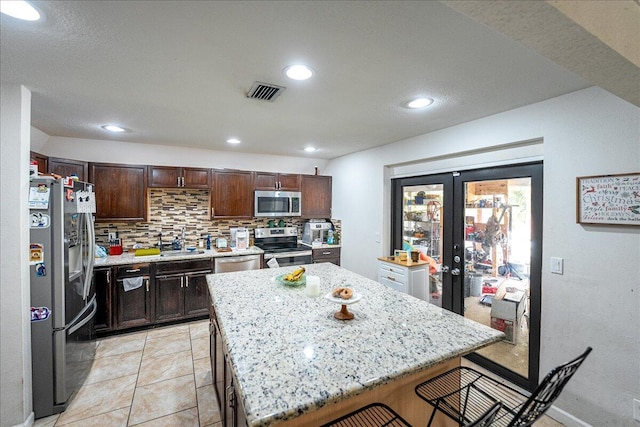 kitchen featuring french doors, a kitchen bar, a center island, stainless steel appliances, and decorative backsplash