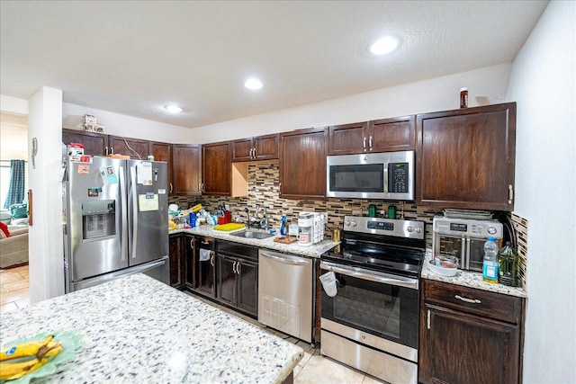 kitchen featuring sink, tasteful backsplash, light stone counters, dark brown cabinets, and stainless steel appliances