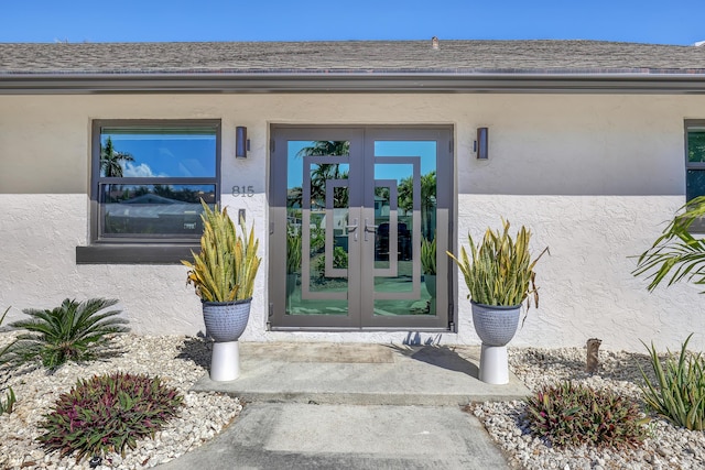 view of exterior entry with a shingled roof, french doors, and stucco siding