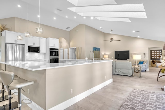 kitchen with black microwave, white cabinetry, light countertops, stainless steel refrigerator, and a large island with sink