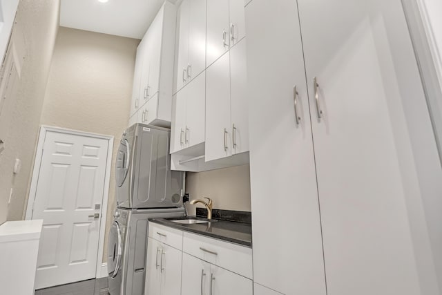 kitchen with dark countertops, white cabinets, a sink, and stacked washing maching and dryer