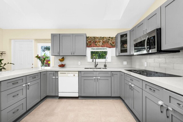 kitchen featuring sink, appliances with stainless steel finishes, gray cabinets, kitchen peninsula, and backsplash