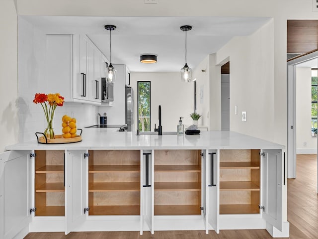 kitchen with a peninsula, a sink, white cabinets, stainless steel microwave, and pendant lighting