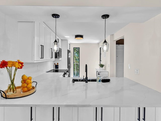 kitchen featuring appliances with stainless steel finishes, white cabinetry, a sink, light stone countertops, and a peninsula