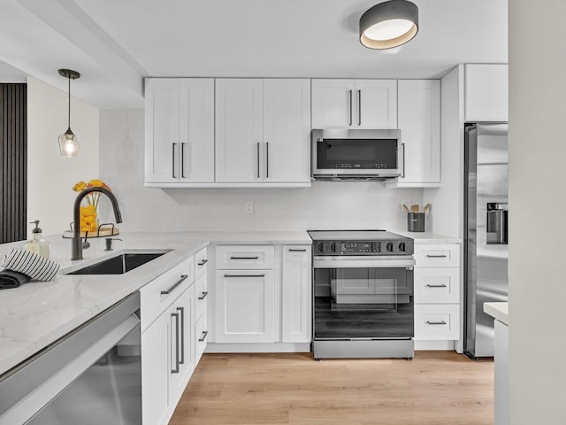 kitchen with white cabinetry, sink, hanging light fixtures, stainless steel appliances, and light wood-type flooring