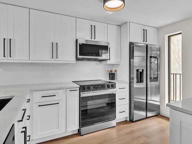 kitchen with white cabinetry, stainless steel appliances, light stone countertops, light hardwood / wood-style floors, and decorative backsplash