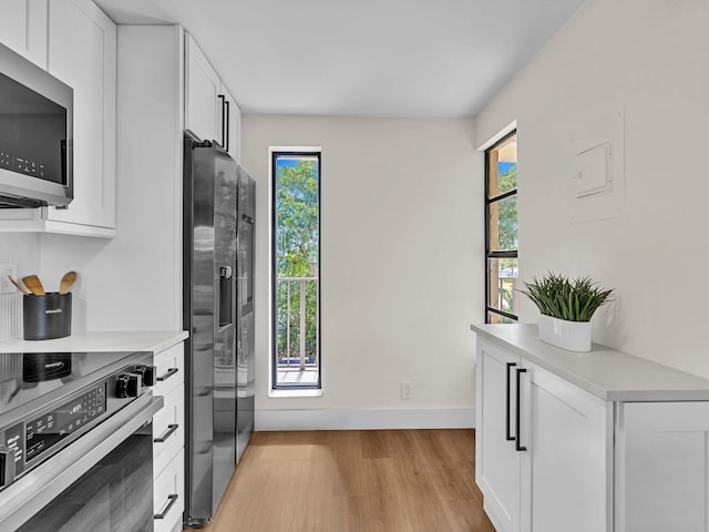 kitchen featuring stainless steel appliances, white cabinetry, baseboards, light countertops, and light wood-type flooring