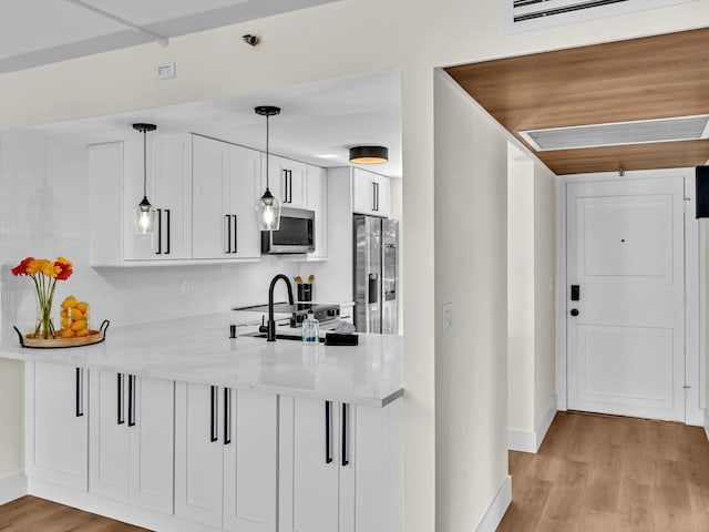 kitchen with light hardwood / wood-style flooring, appliances with stainless steel finishes, white cabinetry, decorative light fixtures, and kitchen peninsula