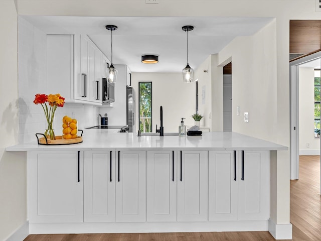 kitchen featuring a peninsula, a sink, white cabinetry, appliances with stainless steel finishes, and decorative light fixtures