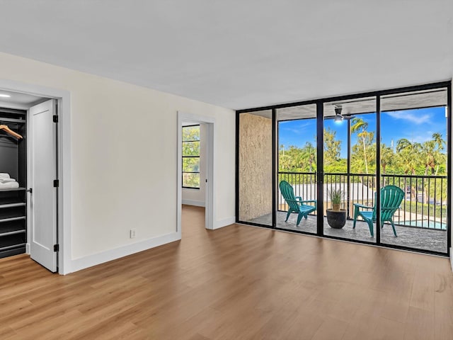 spare room featuring a wall of windows, baseboards, and wood finished floors