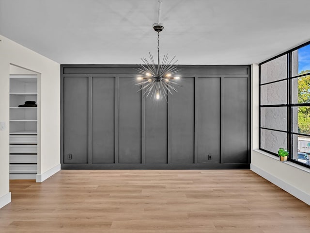 interior space featuring baseboards, light wood-style floors, an inviting chandelier, and a decorative wall