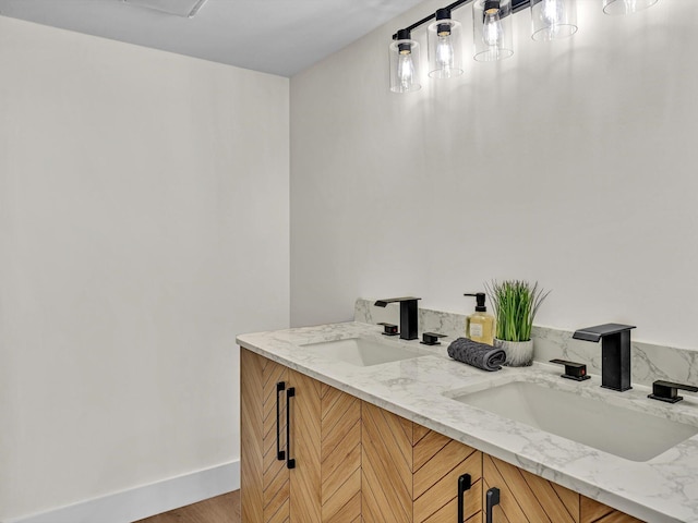 bathroom with wood finished floors, a sink, baseboards, and double vanity