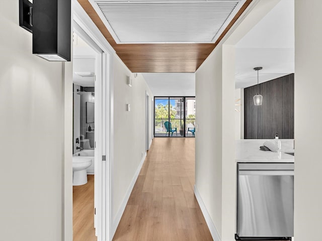 hall with expansive windows, baseboards, and light wood finished floors