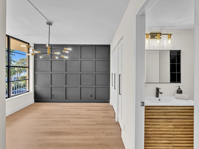 unfurnished dining area featuring light wood-style floors, an inviting chandelier, a sink, and a decorative wall