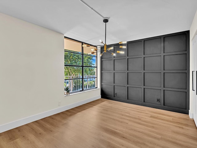 interior space with a chandelier, a decorative wall, baseboards, and wood finished floors