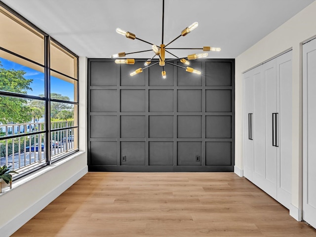 unfurnished dining area with a chandelier, baseboards, wood finished floors, and a decorative wall