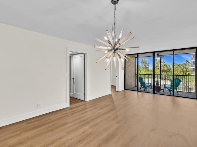 spare room with an inviting chandelier, a wall of windows, and light hardwood / wood-style floors