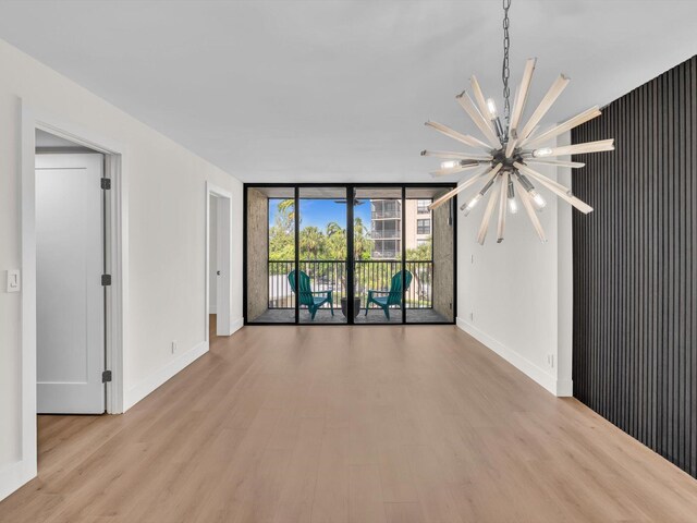 empty room with light wood-type flooring, a chandelier, and a wall of windows