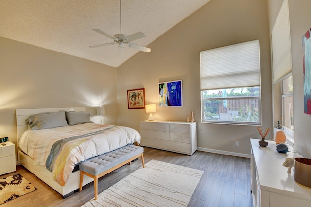 bedroom with ceiling fan, hardwood / wood-style flooring, high vaulted ceiling, and a textured ceiling