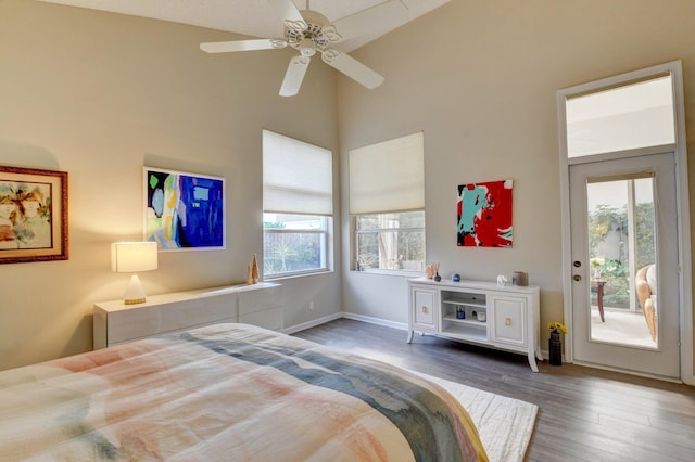 bedroom with dark hardwood / wood-style floors, a towering ceiling, access to exterior, and multiple windows