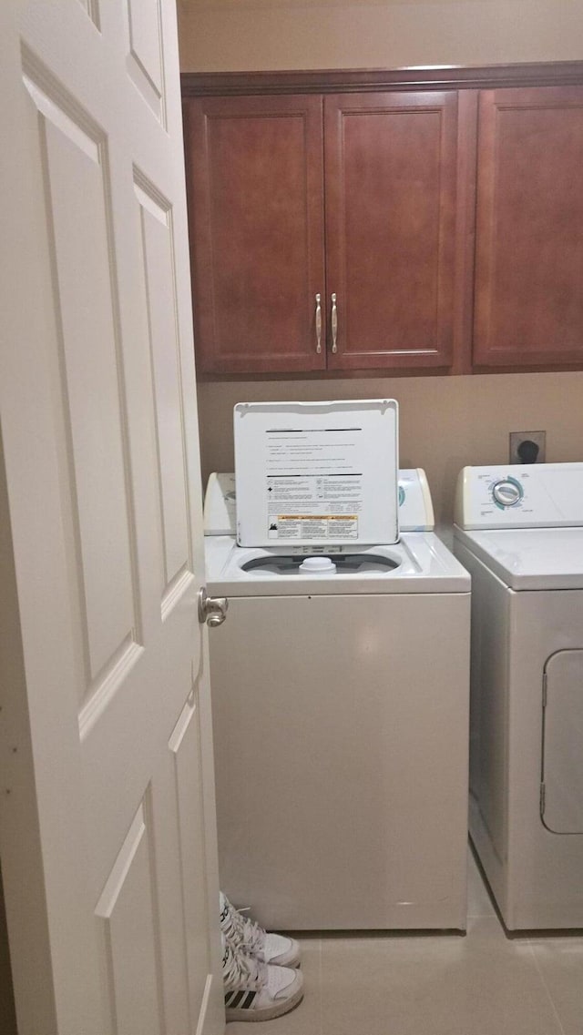 clothes washing area with cabinet space, light tile patterned floors, and washing machine and clothes dryer