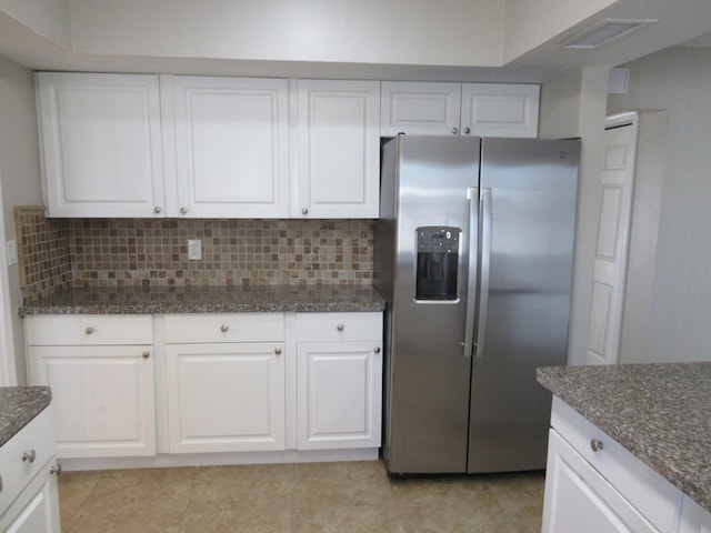 kitchen with white cabinetry, tasteful backsplash, light tile patterned floors, stainless steel fridge, and dark stone counters