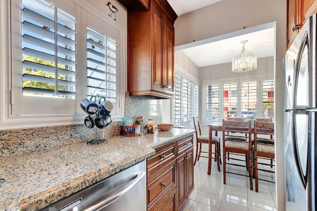 kitchen with appliances with stainless steel finishes, pendant lighting, backsplash, light stone counters, and an inviting chandelier