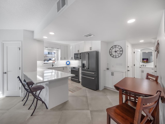 kitchen with a breakfast bar, sink, white cabinetry, tasteful backsplash, and stainless steel appliances