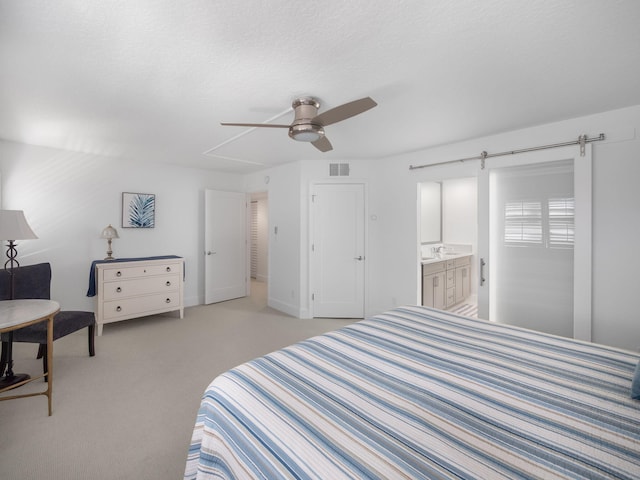 bedroom with ensuite bathroom, light colored carpet, ceiling fan, a barn door, and a textured ceiling