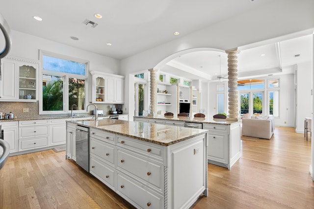 kitchen with light stone countertops, an island with sink, kitchen peninsula, and white cabinets