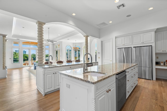 kitchen featuring sink, decorative columns, stainless steel appliances, a kitchen island with sink, and white cabinets